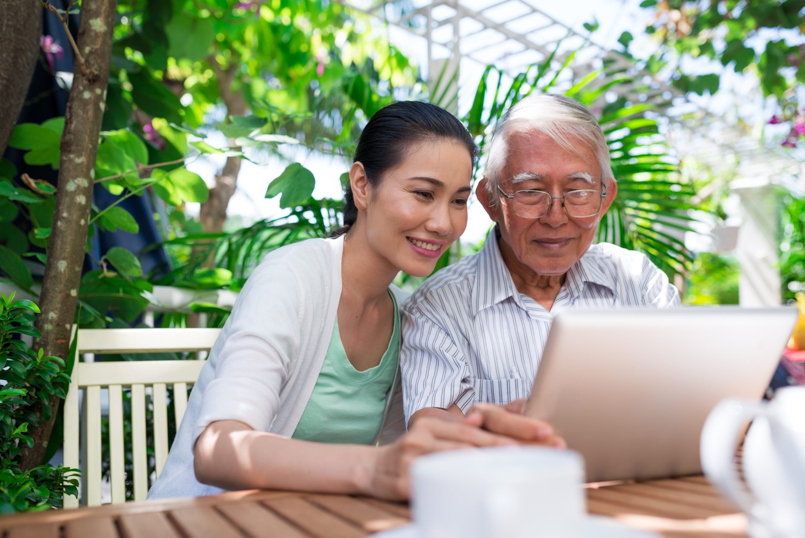 Cheerful Vietnamese father and daughter sitting in outdoor cafe and watching something on tablet