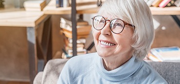 An elderly woman in glasses and a turtleneck smiling
